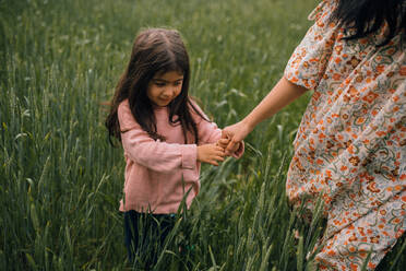 Smiling girl holding moms hand while walking in field - CAVF91986