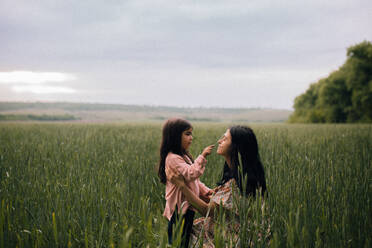 Lächelnde Mutter und Tochter, die sich auf einem Feld unterhalten - CAVF91991