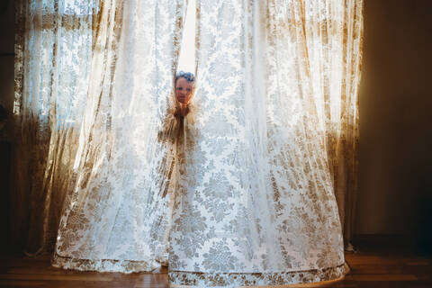 Little girl playing hide and seek with big vintage curtains at home stock photo