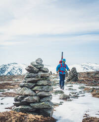 Mann folgt Steinmännchen über Schnee und Eis mit Skiern auf dem Rücken - CAVF92019