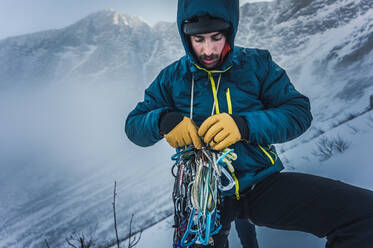 Ein Mann sortiert während einer Wintertour seine Kletterausrüstung aus Fels und Eis - CAVF92020