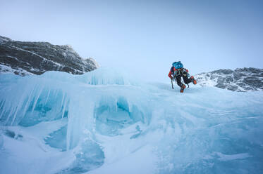 Ein Kletterer befreit ein Stück Eis in Maine neben einem Sonnenschirm - CAVF92021