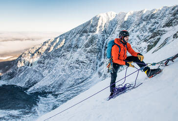 Ein männlicher Kletterer sichert einen anderen Kletterer während einer alpinen Eiskletterei im Winter - CAVF92022