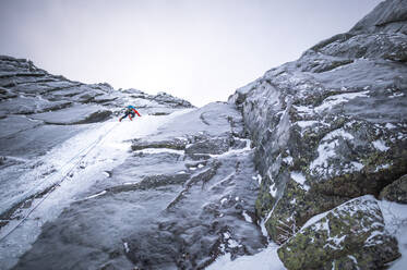 Ein alpiner Eiskletterer, der einen steilen Abschnitt eines großen Berges erklimmt - CAVF92024