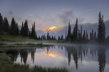 Mount Rainier, der am frühen Morgen bei Sonnenaufgang durch die Wolken blickt - CAVF92040