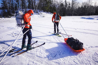 Zwei Männer befestigen auf einem verschneiten Parkplatz Pulkschlitten an ihren Rucksäcken - CAVF92058