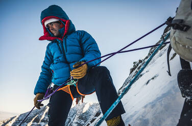 Male climber belays his lead climber during a cold winter alpine climb - CAVF92061