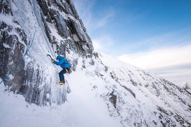 An alpine climber being belayed up a steep section of ice with mountains behind - CAVF92064