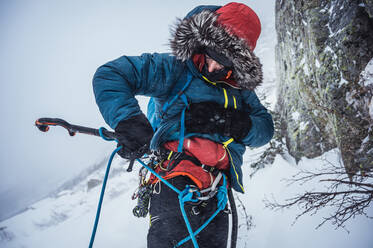 Ein Mann befestigt bei einer Eisklettertour im Winter ein Eisgerät an seinem Klettergurt - CAVF92068
