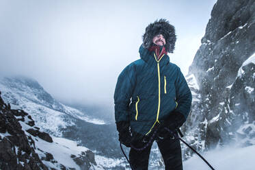 Ein männlicher Bergsteiger sichert seinen Vorsteiger bei Schneetreiben in der Kälte - CAVF92071