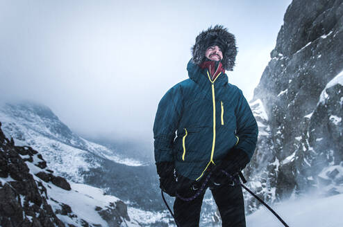 Male alpine climber belays his lead climber as snow blows in the cold - CAVF92071