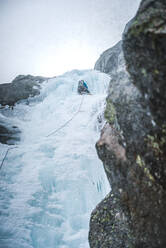 An ice climber climbs up a steep gully full of ice in Maine alpine - CAVF92073