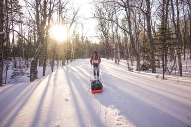 Skier pulling pulk sled on a trail at sunrise - CAVF92077