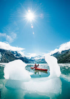 Woman kayaking in Glacier Bay National Park with iceberg in foreground - CAVF92090