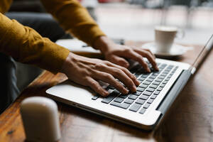 Junger Mann arbeitet am Laptop, während er im Café sitzt - EGAF01452