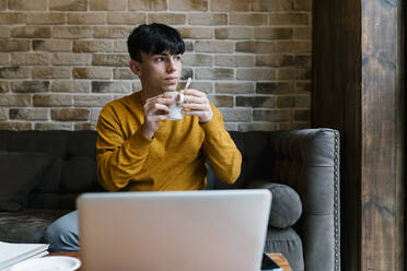 Mann mit Laptop trinkt Kaffee, während er auf dem Sofa im Café sitzt - EGAF01455