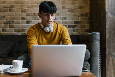 Mann mit Kopfhörern, der im Café sitzend am Laptop arbeitet - EGAF01458