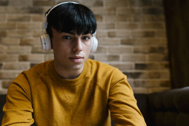 Junger Mann mit Kopfhörern, der im Café sitzt und starrt - EGAF01459