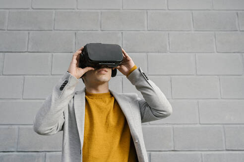 Mann benutzt ein Virtual-Reality-Headset, während er vor einer grauen Wand steht - EGAF01466