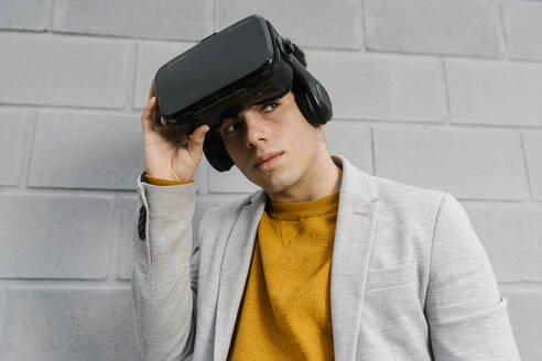 Man removing virtual reality headset while standing against gray wall - EGAF01469