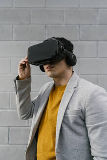 Mann mit Virtual-Reality-Headset vor einer grauen Wand - EGAF01470