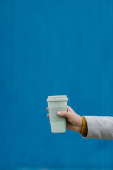 Man holding disposable cup against blue wall - EGAF01473
