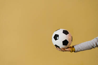 Junger Mann hält Fußball gegen gelbe Wand - EGAF01481