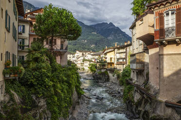 Fluss Mera inmitten von Gebäuden in der Stadt gegen den Berg, Valchiavenna, Chiavenna, Provinz Sondrio, Lombardei, Italien - MAMF01554