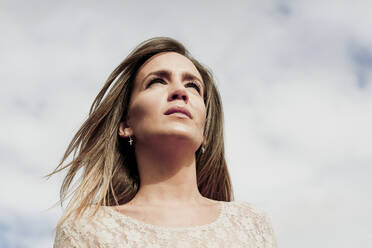 Close-up of thoughtful woman with blond hair against cloudy sky - ERRF04904