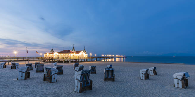 Deutschland, Mecklenburg-Vorpommern, Heringsdorf, Strandkörbe mit Kapuze am leeren Strand in der Abenddämmerung mit der beleuchteten Seebrücke Ahlbeck im Hintergrund - WDF06495