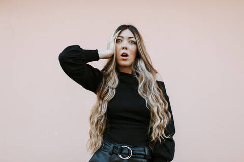 Shocked young woman with head in hand standing against wall stock photo