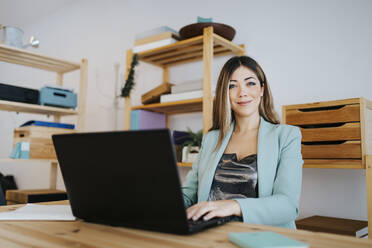 Lächelnde Geschäftsfrau arbeitet an einem Laptop auf einem Schreibtisch im Büro - MIMFF00480