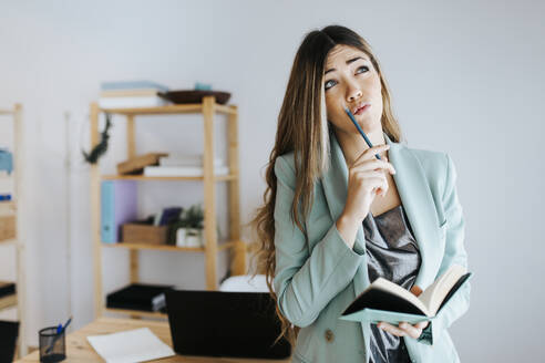 Geschäftsfrau denkt beim Schreiben in Tagebuch im Büro - MIMFF00482