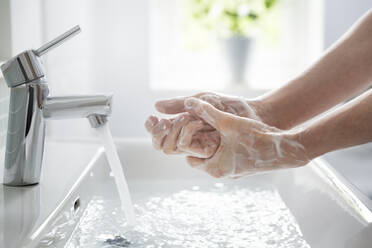 Close up teenage boy washing hands with soap and water at sink - CAIF30200