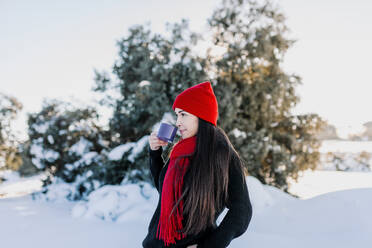 Frau trinkt Kaffee, während sie auf einem verschneiten Grundstück in der Natur steht - MRRF00825