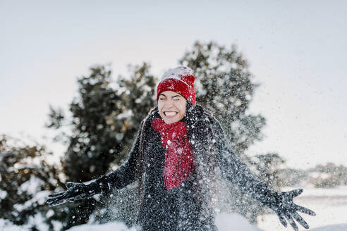 Smiling woman throwing snow while enjoying vacation at countryside - MRRF00831