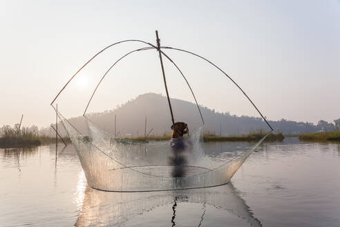 Fischer auf seinem Boot, der auf dem Loktak-See bogenförmige Stellnetze über dem Wasser bewegt - MINF15708