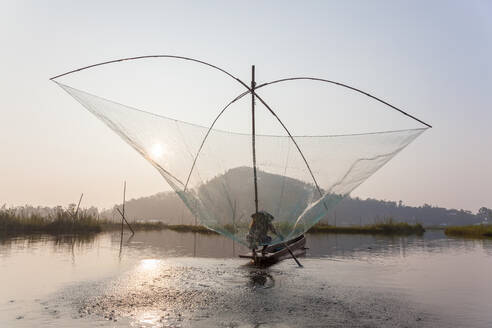 Fischer auf seinem Boot, der auf dem Loktak-See bogenförmige Stellnetze über dem Wasser bewegt - MINF15709