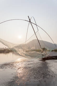 Fischer auf seinem Boot, der auf dem Loktak-See bogenförmige Stellnetze über dem Wasser bewegt - MINF15710