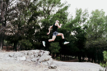 Male athlete jumping over rock on mountain - EBBF02272