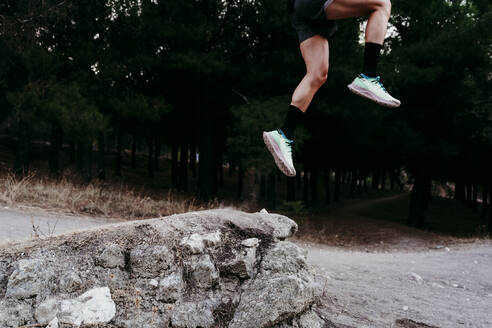 Junger männlicher Sportler springt über einen Felsen am Berg - EBBF02274