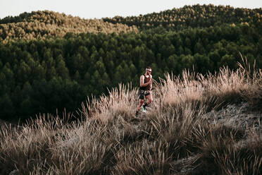 Male athlete running on mountain in dried grass - EBBF02287