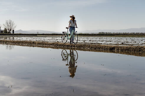 Junge Frau steht mit Fahrrad gegen den Himmel am Ebro-Delta während der Ferien, Spanien - AFVF08063