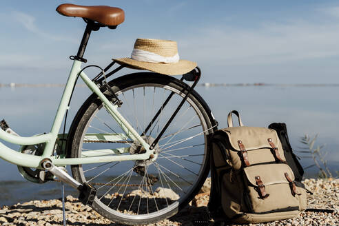 Rucksack auf Fahrrad gelehnt mit Hut am Ebro-Delta gegen den Himmel an einem sonnigen Tag, Spanien - AFVF08066