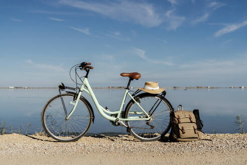 Abgestelltes Fahrrad mit Rucksack auf dem Hinterrad und Hut an einem sonnigen Tag im Ebro-Delta, Spanien - AFVF08068