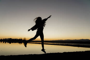 Carefree young woman with arms raised dancing during dusk at Ebro Delta, Spain - AFVF08078