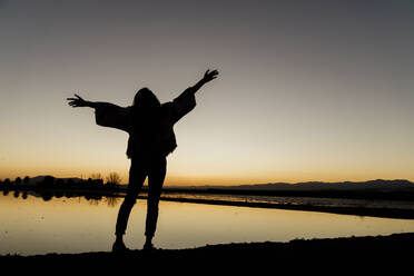 Young woman with arms outstretched standing by river during dusk at Ebro delta, Spain - AFVF08079