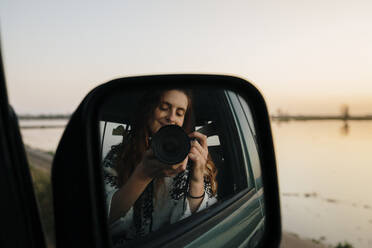 Young woman photographing self on side-view mirror reflection through camera at Ebro Delta - AFVF08085