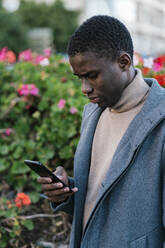 Mann in Jacke, der ein Mobiltelefon benutzt, während er im Park steht - EGAF01497