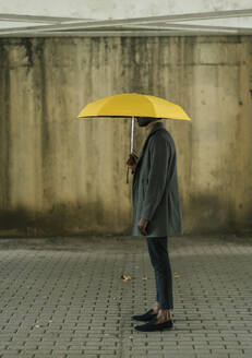 Mann im Mantel mit Regenschirm auf dem Fußweg stehend - EGAF01506